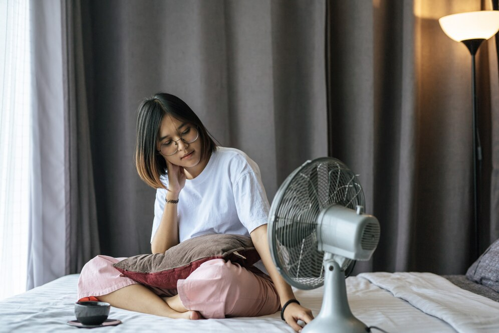 Person sleeping peacefully in a cool bedroom with a fan nearby, illustrating the importance of temperature regulation for better sleep.