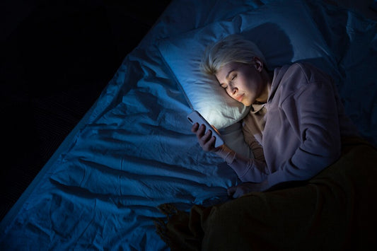 "Person lying in bed in the dark, illuminated by the glow of a smartphone screen, illustrating the impact of blue light on sleep.